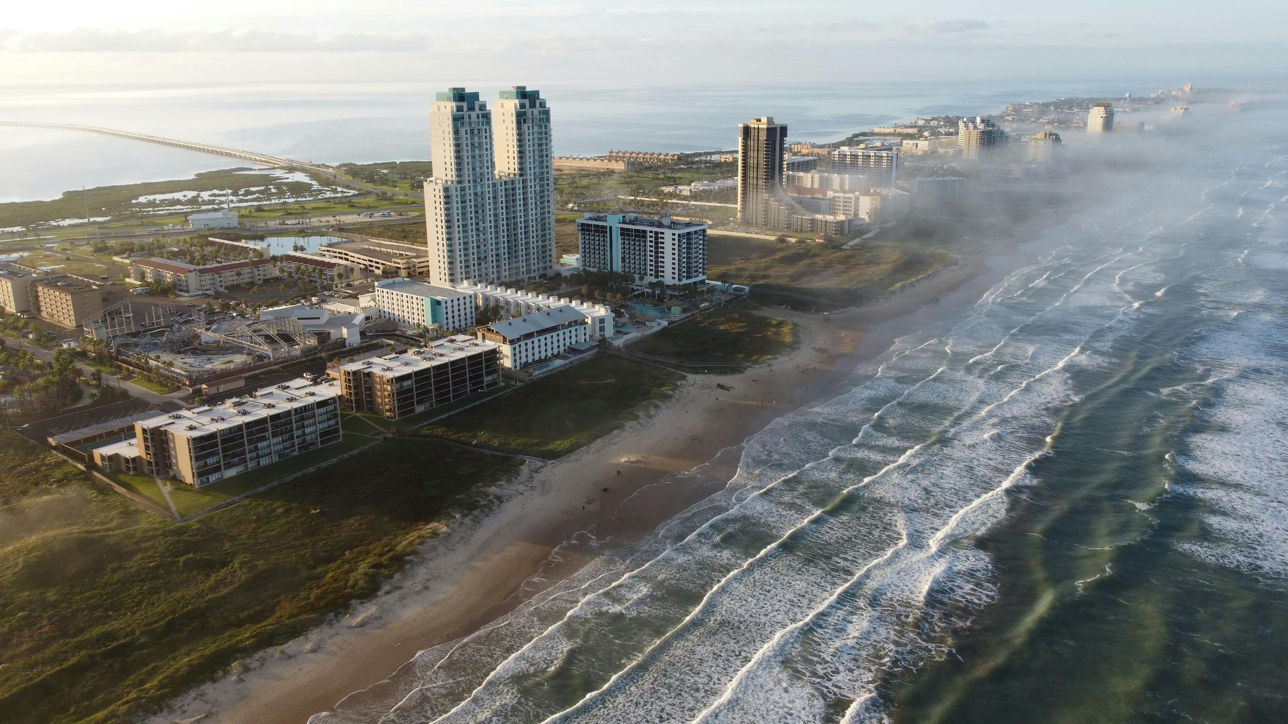 Sunrise aerial of South Padre Island's coastline with tall buildings and waves.